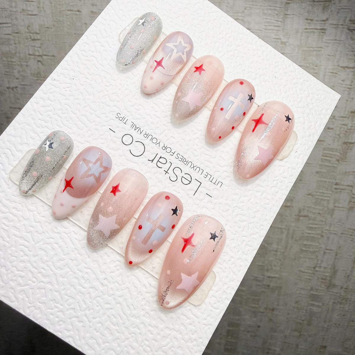 A collection of beautifully manicured nails with various star and star-shaped designs, including red and white stars, on a white background.
