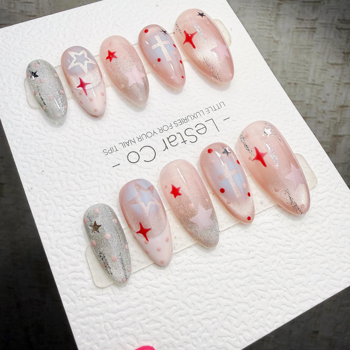 A collection of beautifully manicured nails with various star and star-shaped designs, including glitter and metallic accents, displayed on a white surface.