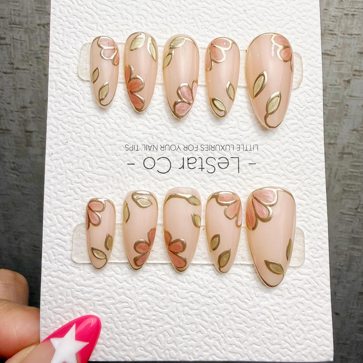 A set of pink nail art designs featuring leaves and flowers, with a hand holding the nail art display.