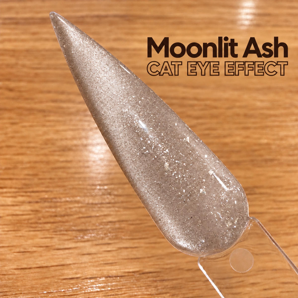 A close-up image of a glittery nail polish bottle on a wooden surface, with text above it that reads "Moonlit Ash CAT Eye Effect".
