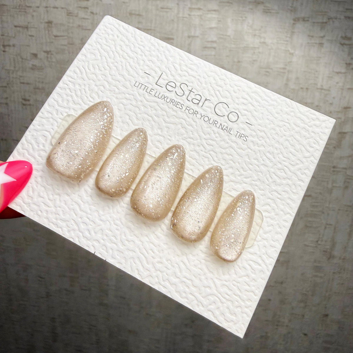 A hand holding a white card with a row of glittery nail polish bottles on it.