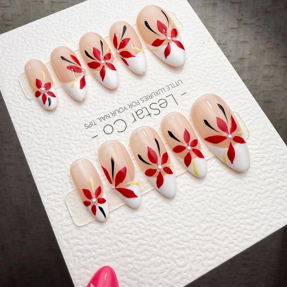A set of elaborately decorated fingernails with floral designs, displayed on a white surface.