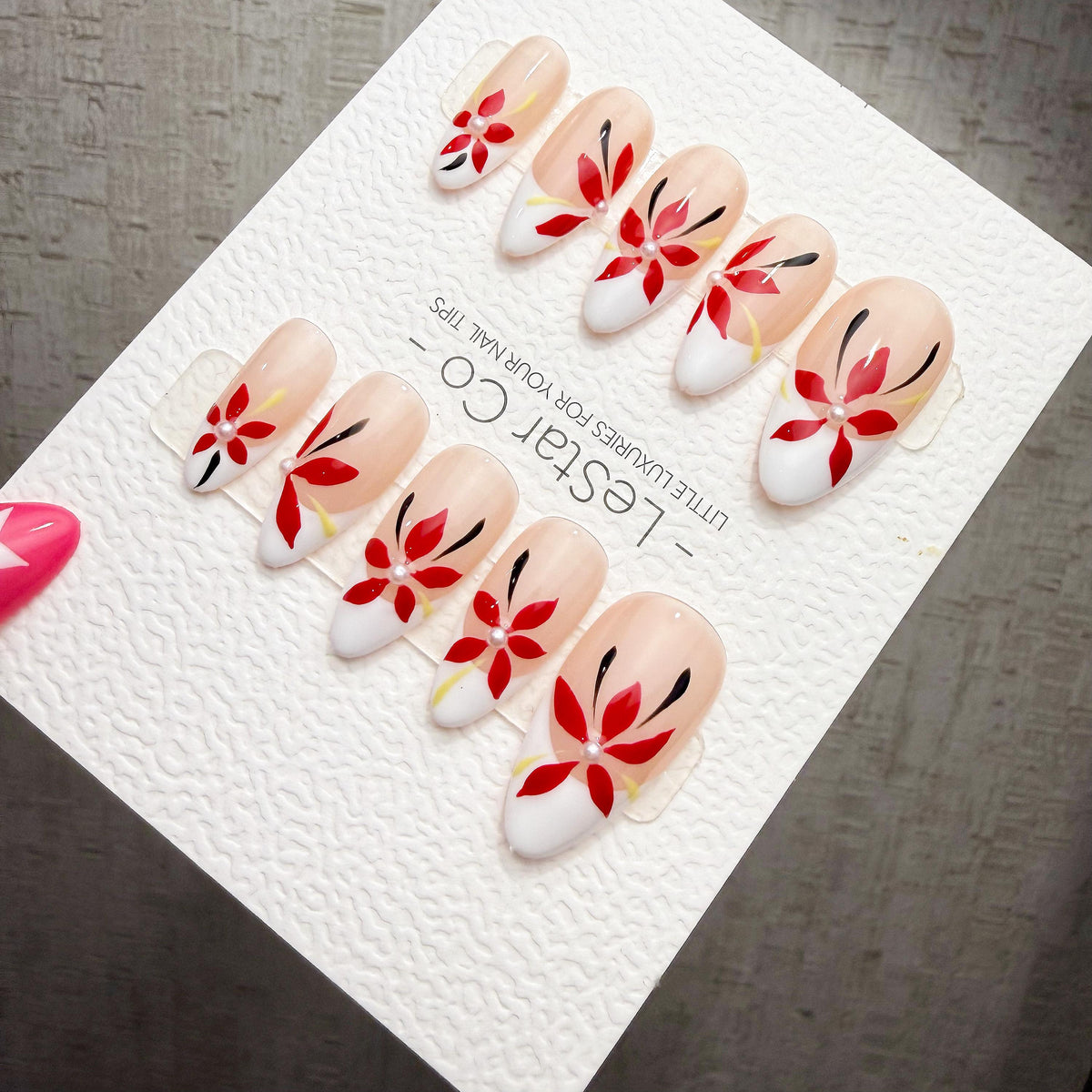 A set of elaborately decorated fingernails with red and white floral designs.