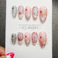 A set of elaborately decorated nails with various designs, including stars, crosses, and polka dots, displayed on a white background.