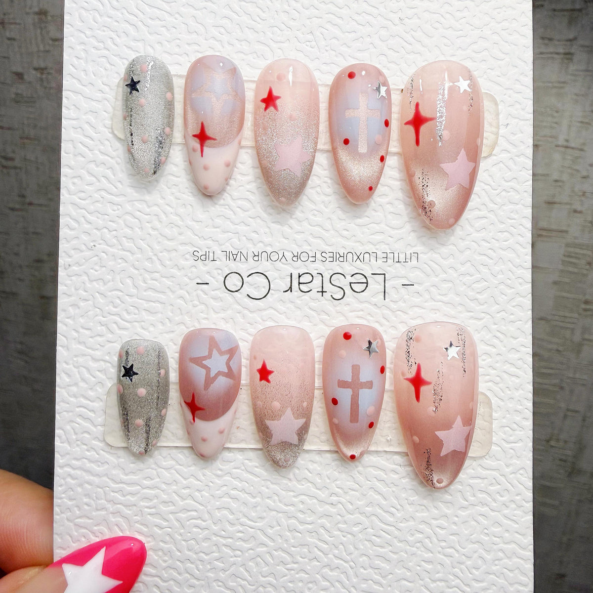A set of elaborately decorated nails with various designs, including stars, crosses, and polka dots, displayed on a white background.