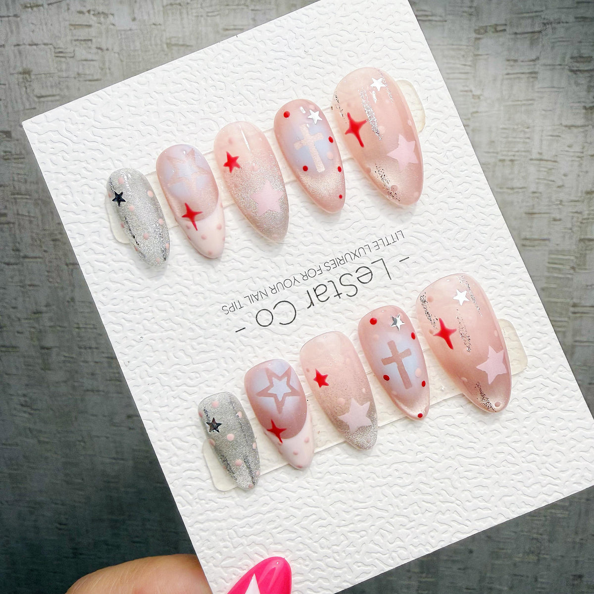 A hand holding a card with various nail art designs, including stars, crosses, and glittery elements.
