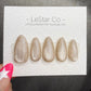 A set of gold glittery nail tips is displayed on a white background, with a hand holding the product.