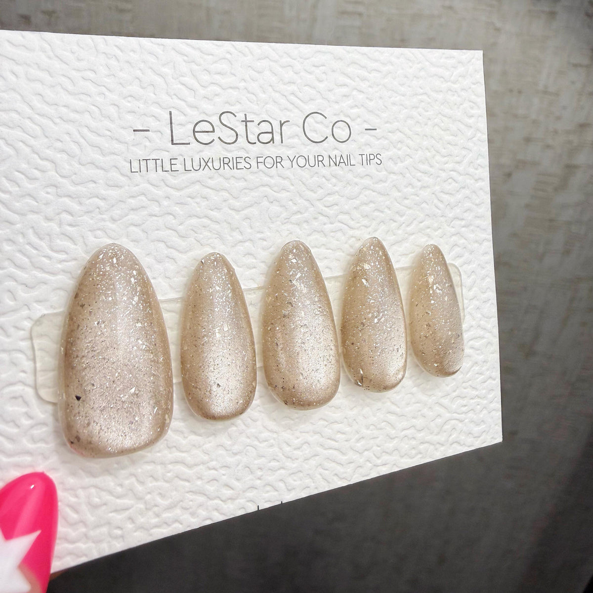 A close-up of a nail art product packaging with a set of gold glittery nail tips displayed on it.