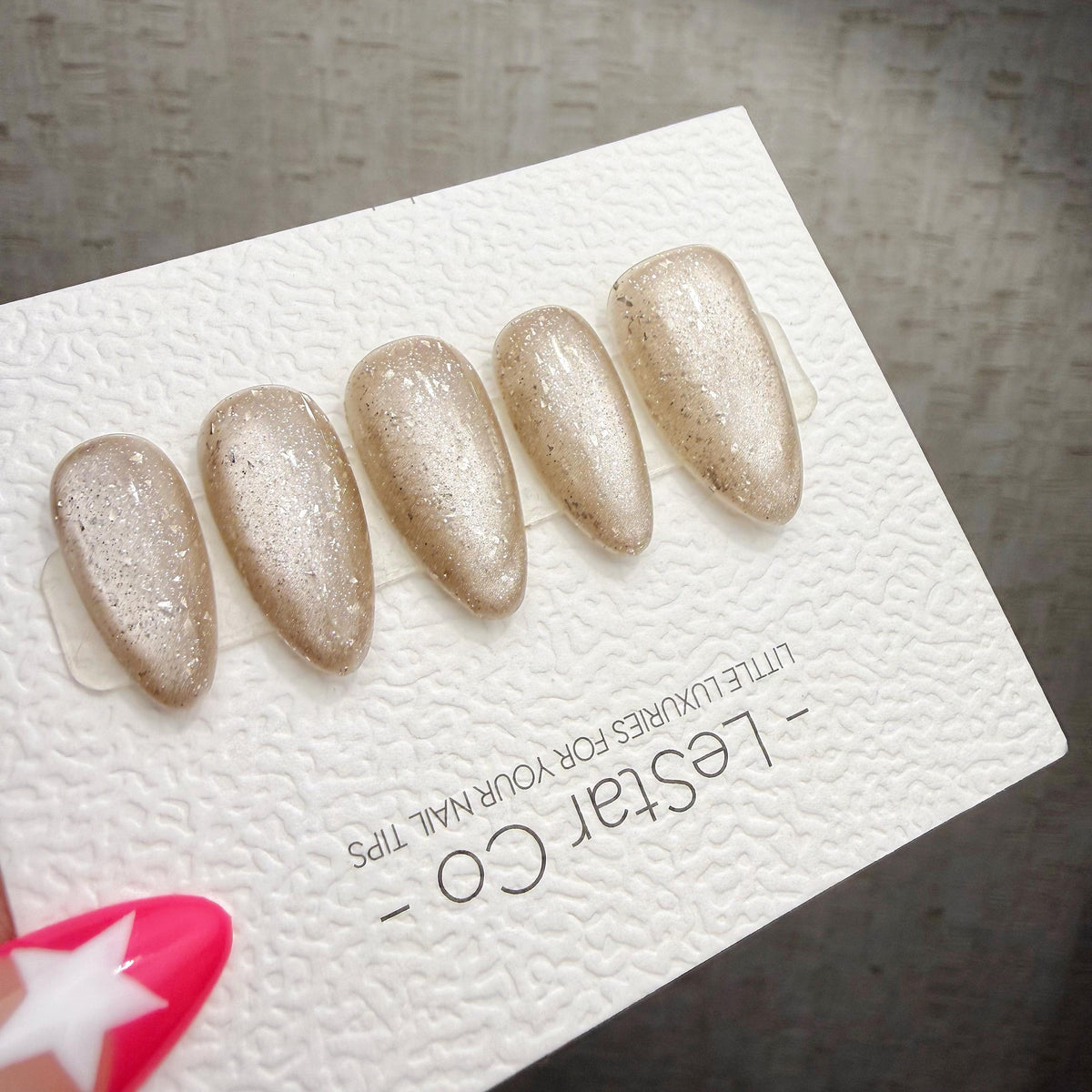 A close-up of a white card with text and images of glittery nail art designs.